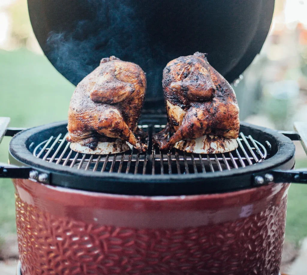 2 whole chickens on ceramic chicken stands sit next to each other on the grate of an open Kamado Joe grill. Both chickens are roasted golden brown with crispy bits here and there. 